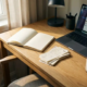 Opgeruimd eiken bureau met open notitieboek, bonnetjes, halfopen laptop en koffiekopje in warm ochtendlicht.