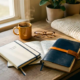Freelance thuiswerkplek met slanke tweejarenplanner en dikke meerjarenjournal naast dampende koffie en leesbril in warm ochtendlicht.