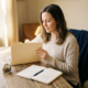 Freelance ondernemer bekijkt factuurmap aan minimalistisch houten bureau, met spaarpot en opengeslagen notitieboek in warm natuurlijk licht.