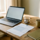 Freelance thuiswerkplek met Nederlands belastingdocument, glazen pot met euromunten en halfopen laptop in warm ochtendlicht.