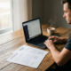 Freelancer aan een thuiswerkplek met overlappende arbeids- en opdrachtovereenkomsten naast een laptop en dampende koffie.