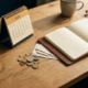 Eiken bureau met 2026-kalender, euromunten, bonnetjes en open leren notitieboek in warm ochtendlicht.
