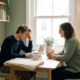 Vermoeide freelancer aan minimalistische thuiswerkplek tegenover een rustige adviseur in warm, natuurlijk verlicht kantoor.