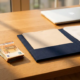 Euro biljetten naast een open belastingmap op een eikenhouten bureau van een freelancer, laptop op de achtergrond.