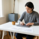 Freelancer aan wit bureau bekijkt twijfelend twee facturen naast gesloten laptop, zacht natuurlijk raamlicht, warme tinten.