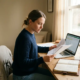 Freelance professional bestudeert financiële documenten aan een modern houten bureau met opengeslagen kasboek en laptop in warm ochtendlicht.