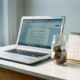 Freelancer laptop en glazen spaarpot met munten op wit bureau naast kalender met weinig boekingen, in zacht natuurlijk licht.