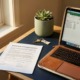 Freelancer laptop en ondertekend verzekeringsdocument op modern bureau, met huissleutel en succulent in warm daglicht.