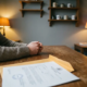 Freelancer aan minimalistisch houten bureau met geopende officiële envelop en overheidsdocument, handen stil in bezorgde rust.