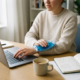 Freelancer aan thuiswerkbureau met laptop en ijspak tegen pijnlijke pols, koffie en notitieboeken op de achtergrond.