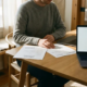Freelancer aan bureau met twee contractdocumenten naast elkaar, laptop open, warm natuurlijk raamlicht en zachte schaduwen.