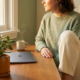 Freelancer aan een zonnig thuiskantoor bureau met dampende koffie, gesloten laptop en een weelderige plant in warm ochtendlicht.