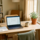 Freelancer thuiskantoor met laptop, bonnetjes, dampende koffie en kamerplant in warm ochtendlicht.