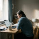 Freelancer staart naar laptop aan minimalistisch houten bureau met onaangeroerd kopje koffie in zacht ochtendlicht.