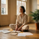 Freelancer zit gekruisbeens op houten vloer in minimalistisch thuiskantoor, omringd door notitieboeken en kamerplant in warm middaglicht.