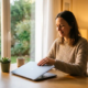 Freelancer sluit laptop aan zonnig thuisbureau met dampende koffie en kamerplant, warme middagzon door raam.