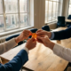 Diverse handen reiken naar een gloeiende munt boven een eiken tafel in een modern Nederlands kantoor, symbool van financiële solidariteit.