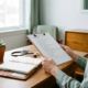 Zelfstandige zorgprofessional bekijkt checklist aan bureau met stethoscoop, agenda en kamerplant in natuurlijk raamlicht.