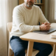 Zelfstandige professional in rust aan minimalistisch thuiskantoor bureau, handen op gesloten laptop naast officiële documenten en koffiemok.