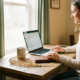 Zelfstandige professional aan houten bureau met laptop en koffie, gouden veiligheidsnet naast notitieboek, warm natuurlijk licht.