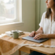 Zelfstandige professional aan minimalistisch thuiskantoor bureau met laptop, notitieboek en koffie op linnengaas, warm amberkleurig licht.
