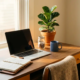 Thuiswerkplek met open agenda, laptop, glazen pot met munten en groen plantje in warm ochtendlicht.