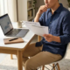 Zelfstandige professional bekijkt verzekeringsdocumenten aan modern thuiskantoor bureau met laptop en notitieboek.