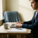 Zelfstandige professional aan minimalistisch thuisbureau met gesloten laptop, medisch attest en koffie in warm natuurlijk licht.