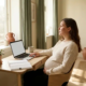 Zwangere freelancer aan Scandinavisch bureau met laptop en planner, hand op buik, zacht middaglicht in thuiskantoor.