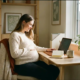 Zwangere freelancer aan thuiskantoor bureau met laptop, hand op buik, warm natuurlijk licht, rustige en zelfverzekerde uitstraling.